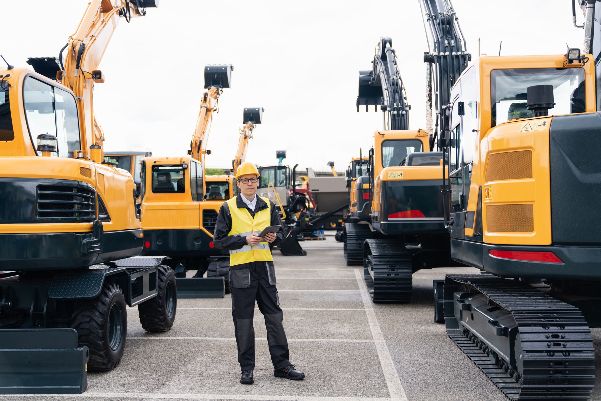 Engineer in a helmet with a digital tablet next to construction excavators