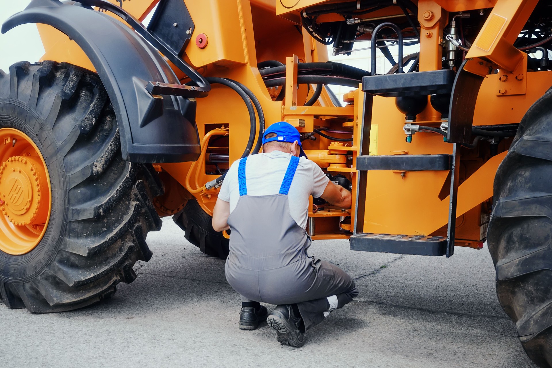 Professional mechanic repairs wheeled tractor or bulldozer. Workshop and maintenance service for agricultural machinery.